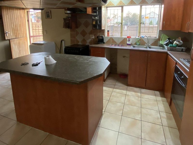 A functional kitchen featuring a central island, built-in cabinetry, double sink, and tiled finishes, offering potential for modernization.