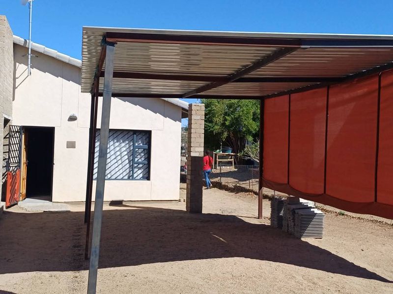 Rear exterior view of the property featuring a covered steel carport structure, security window bars, and an unfinished concrete block wall.