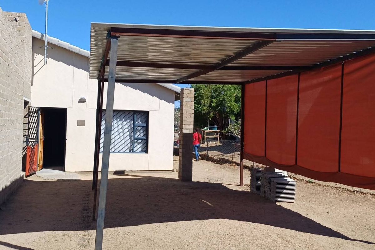 Rear exterior view of the property featuring a covered steel carport structure, security window bars, and an unfinished concrete block wall.