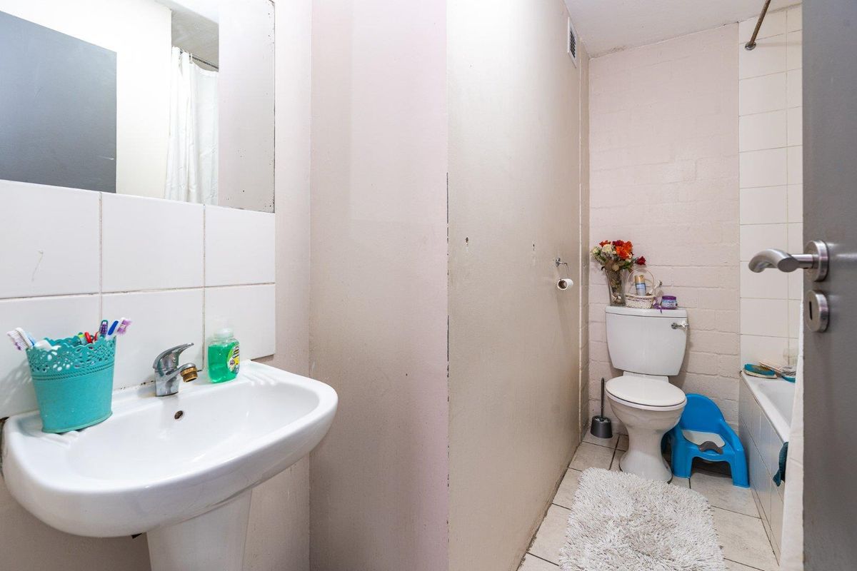 A functional bathroom featuring a pedestal basin, toilet, and a shower-over-bath combination with tiled splashbacks.