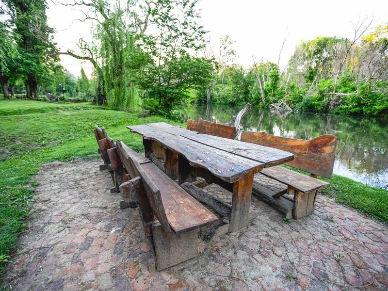 A scenic outdoor garden area featuring a stone-paved seating space situated directly along the riverbank.