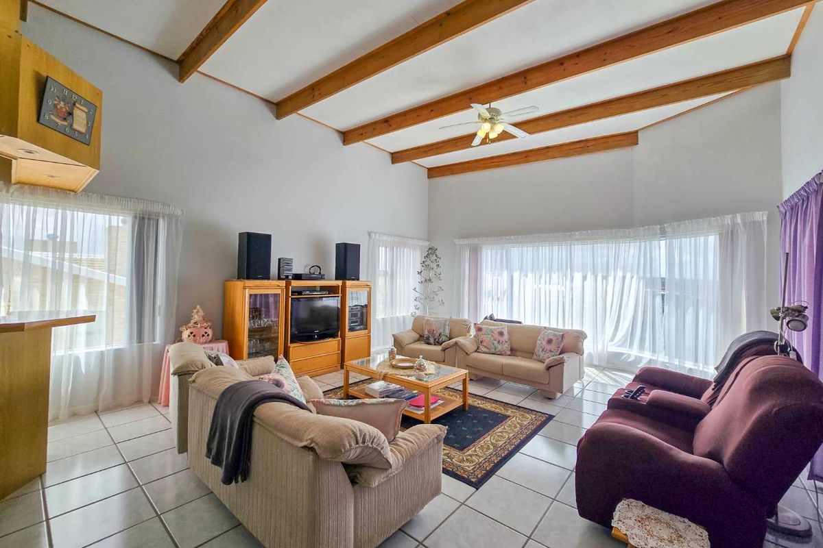 Spacious living room featuring high vaulted ceilings with exposed timber beams, large windows with natural light, and neutral ceramic floor tiles.