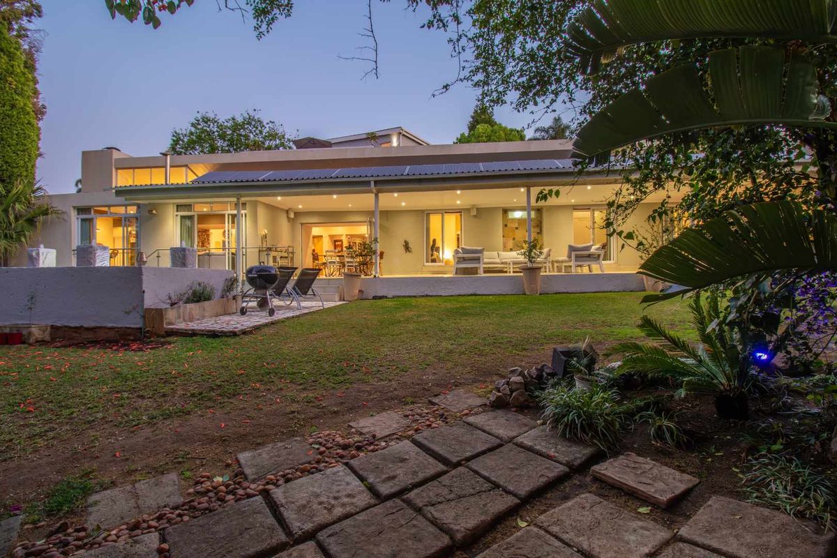 A spacious rear exterior view of the house featuring a covered patio, landscaped garden, and paved walkway leading to the main living area.
