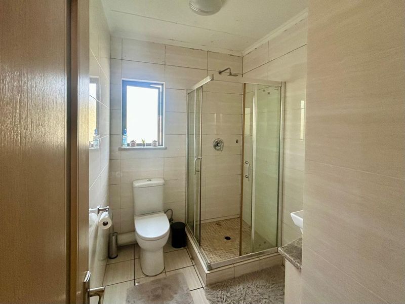 A functional bathroom featuring a glass shower enclosure, toilet, and wall-mounted basin with neutral wall and floor tiling.