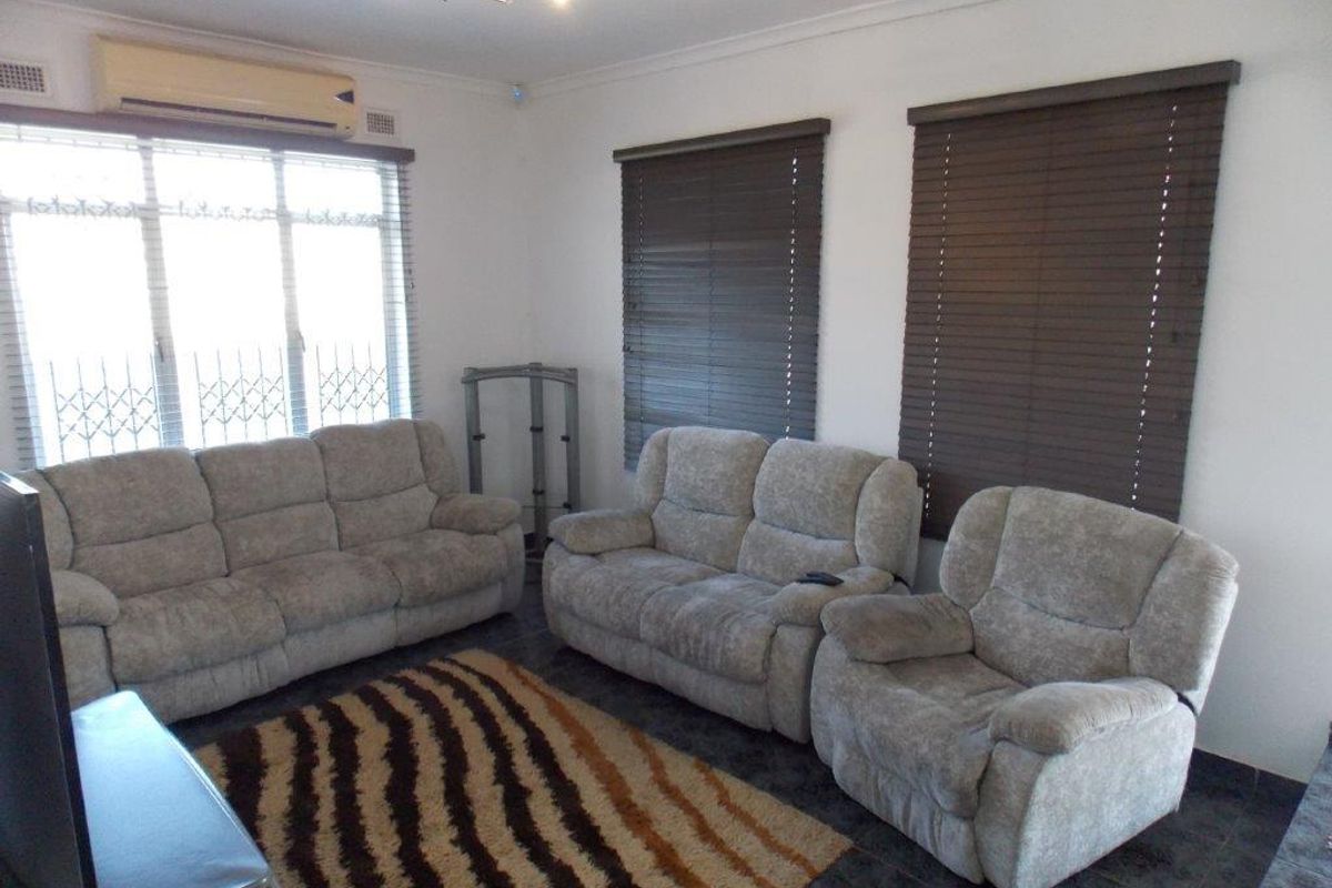A living room featuring tiled flooring, split-system air conditioning, and dark venetian blinds, providing a functional and neutral space for relaxation.