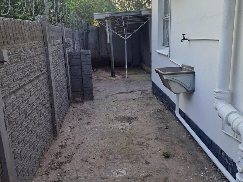 Rear exterior utility area featuring a precast concrete boundary wall with security fencing, an external sink, and basic drainage infrastructure.