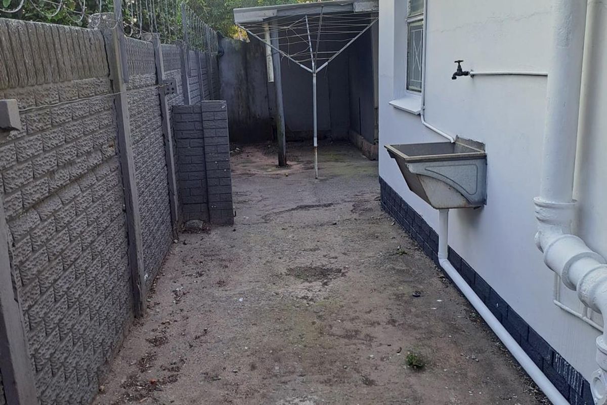 Rear exterior utility area featuring a precast concrete boundary wall with security fencing, an external sink, and basic drainage infrastructure.