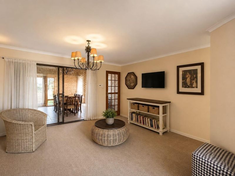 A comfortable living room featuring neutral carpeting, a classic chandelier, and sliding glass doors that provide seamless access to the adjacent covered patio area.