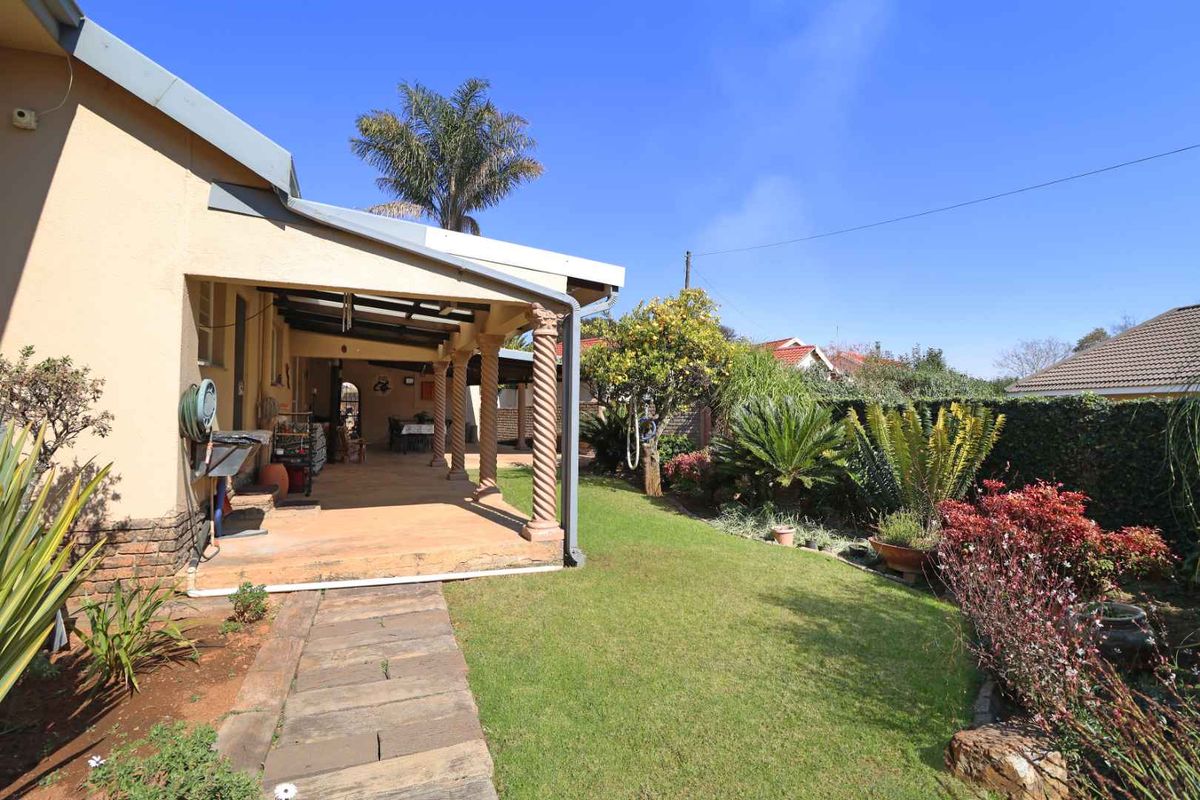 A rear view of the property featuring a covered patio with decorative columns, a paved walkway, and a well-maintained garden area.