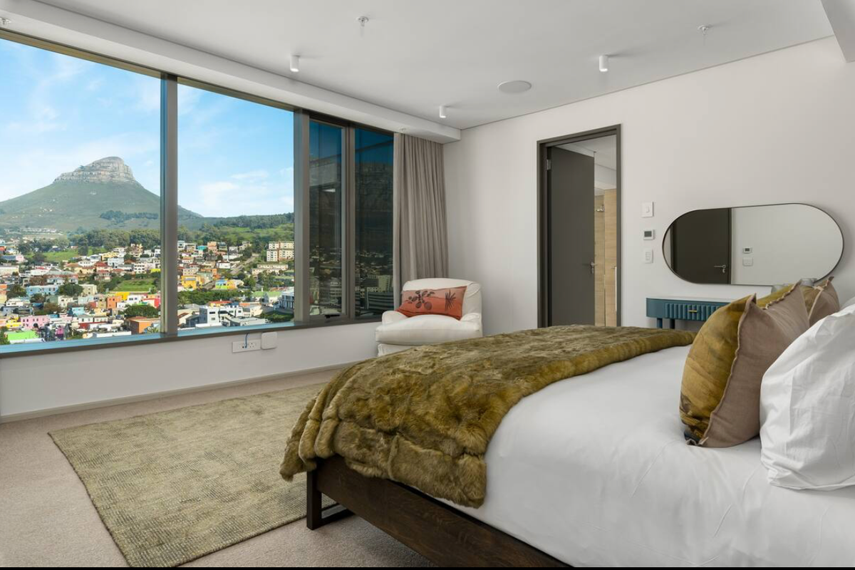 Spacious bedroom featuring floor-to-ceiling windows with panoramic mountain and city views, neutral carpeting, and integrated ceiling lighting.