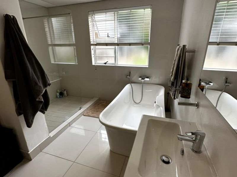 Modern bathroom featuring a freestanding bathtub, a spacious walk-in shower, a vanity basin, and large wall mirrors with neutral tiled finishes.