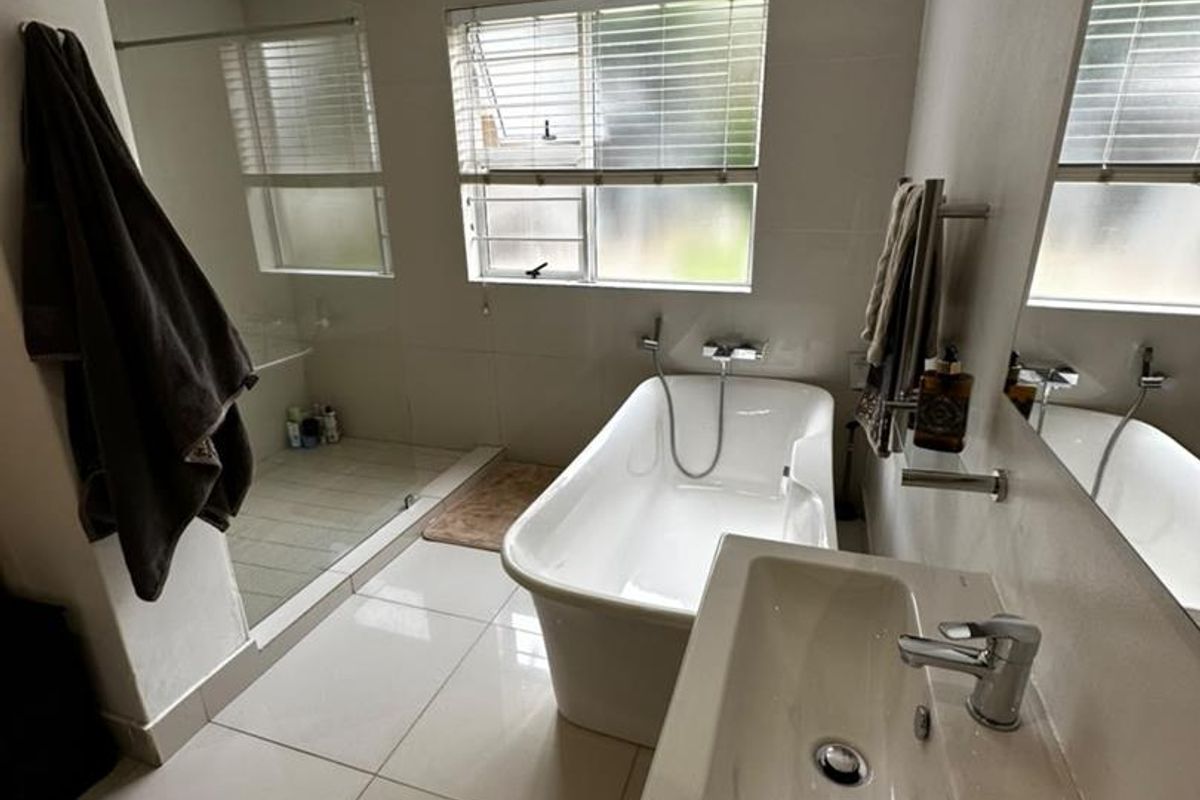 Modern bathroom featuring a freestanding bathtub, a spacious walk-in shower, a vanity basin, and large wall mirrors with neutral tiled finishes.