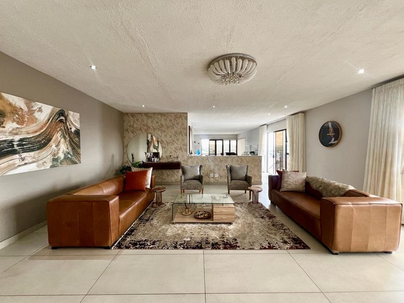 Spacious open-plan living area featuring large format floor tiles, recessed lighting, and a decorative feature wall, seamlessly connecting to the outdoor space.