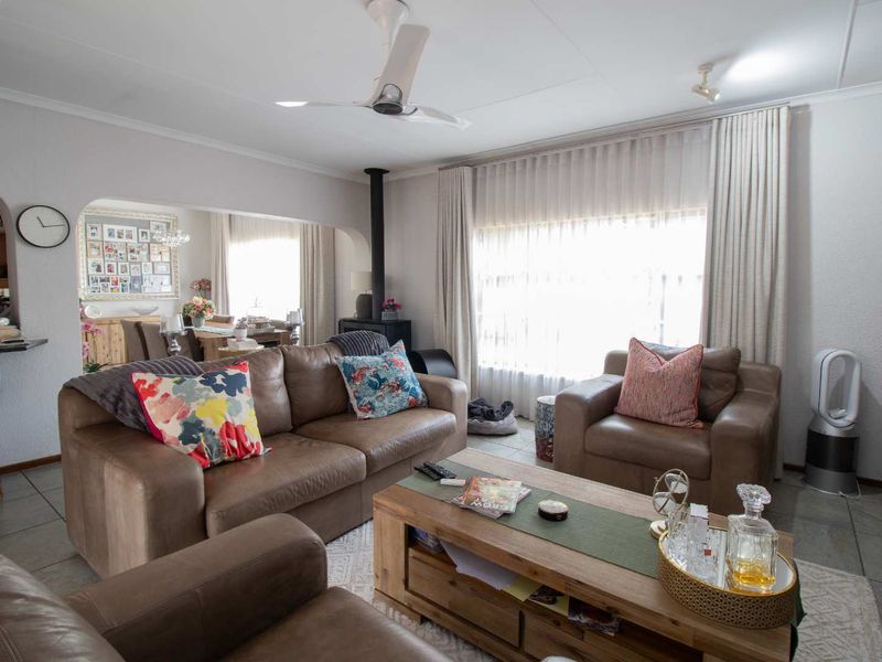 Spacious open-plan living area featuring tiled flooring, a central ceiling fan, and a cozy wood-burning fireplace, seamlessly connecting to the adjacent dining space.