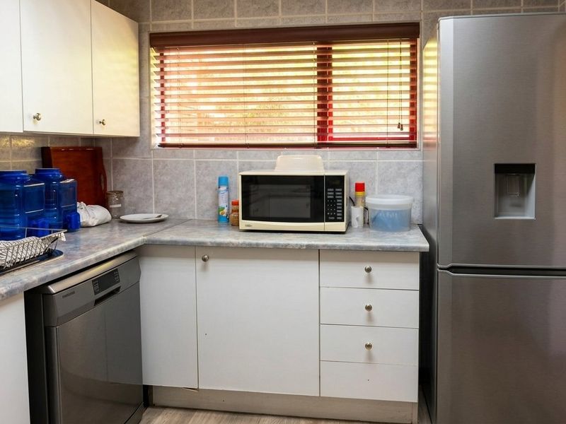A functional kitchen featuring white cabinetry, laminate countertops, tiled backsplash, and a window with venetian blinds.