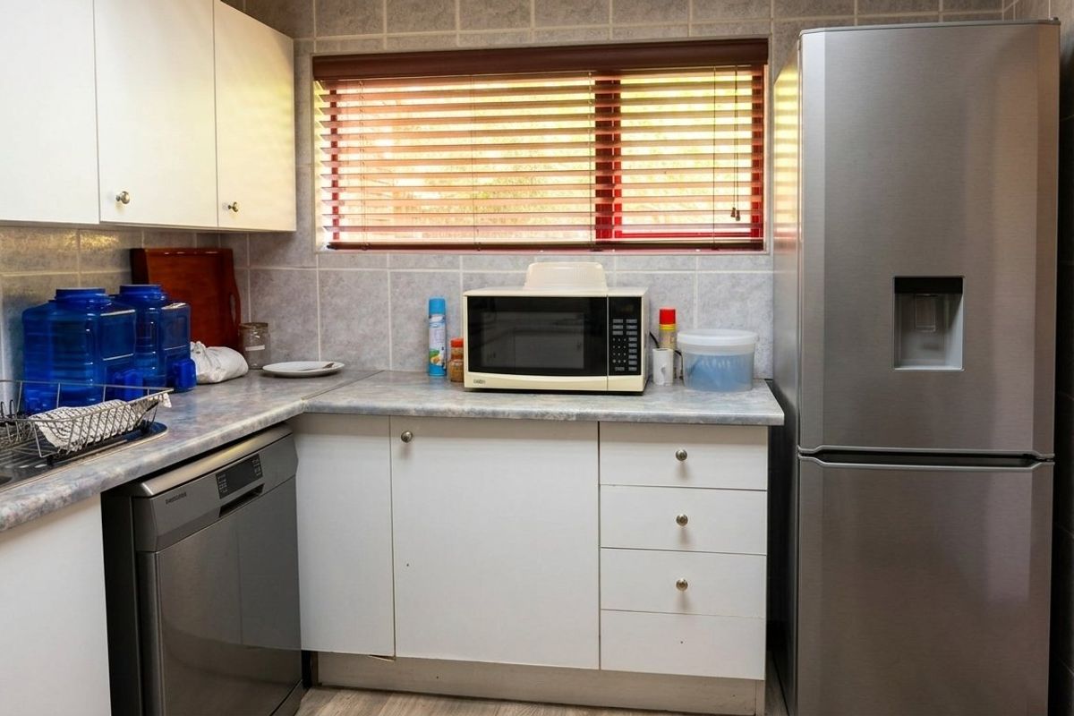 A functional kitchen featuring white cabinetry, laminate countertops, tiled backsplash, and a window with venetian blinds.