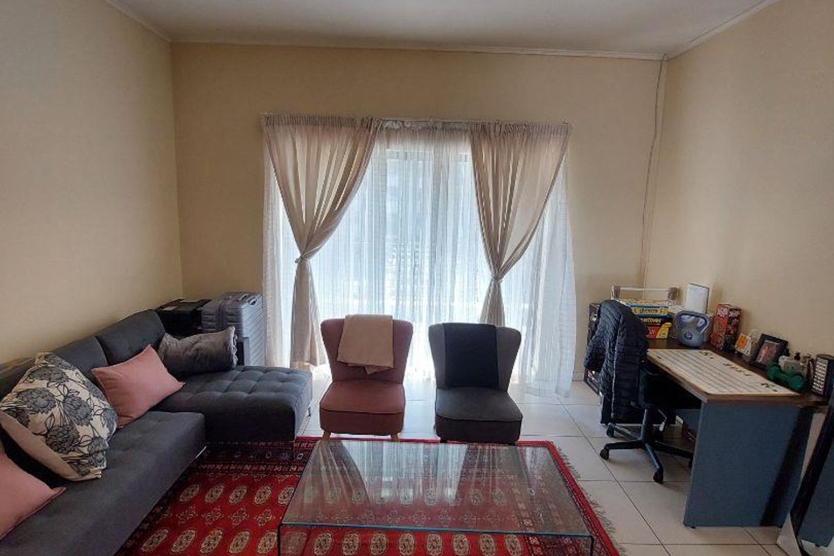 A spacious living room featuring tiled flooring, track lighting, and a large sliding glass door that provides access to the exterior.
