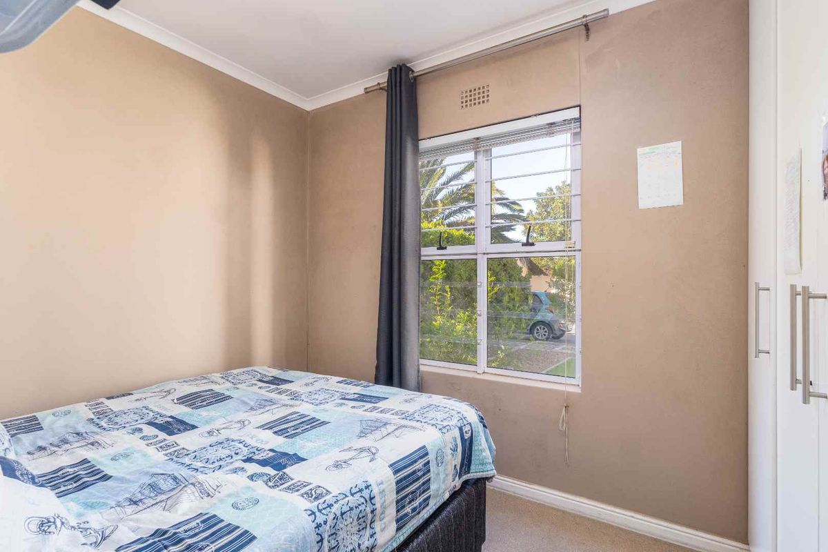 A functional bedroom featuring a built-in wardrobe, neutral wall finishes, and a window fitted with security bars.