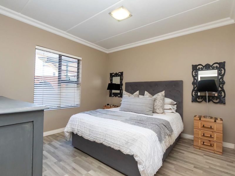 A well-maintained bedroom featuring modern laminate flooring, crown molding, and venetian blinds, offering a clean and comfortable living space.