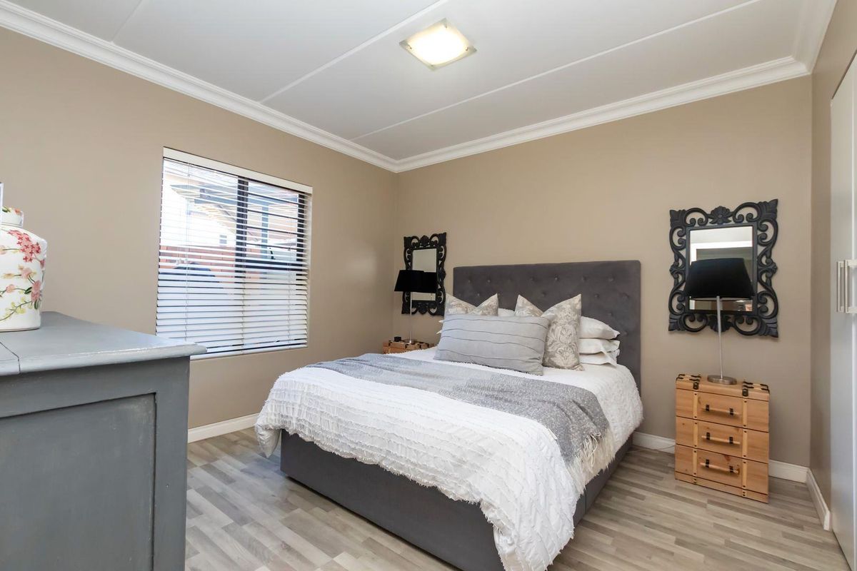A well-maintained bedroom featuring modern laminate flooring, crown molding, and venetian blinds, offering a clean and comfortable living space.