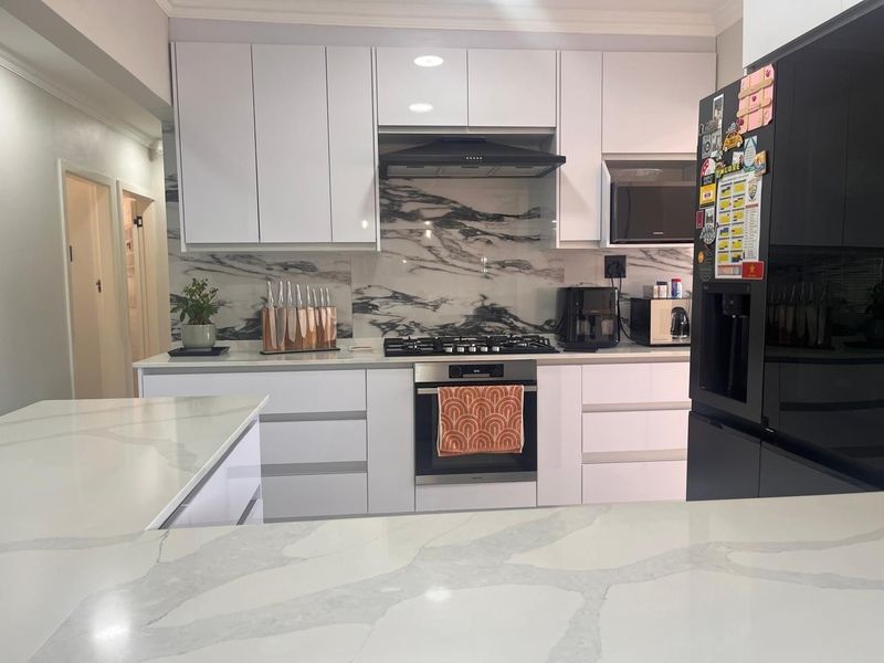Modern kitchen featuring white cabinetry, marble-look quartz countertops and splashback, and integrated stainless steel appliances including a gas hob and oven.