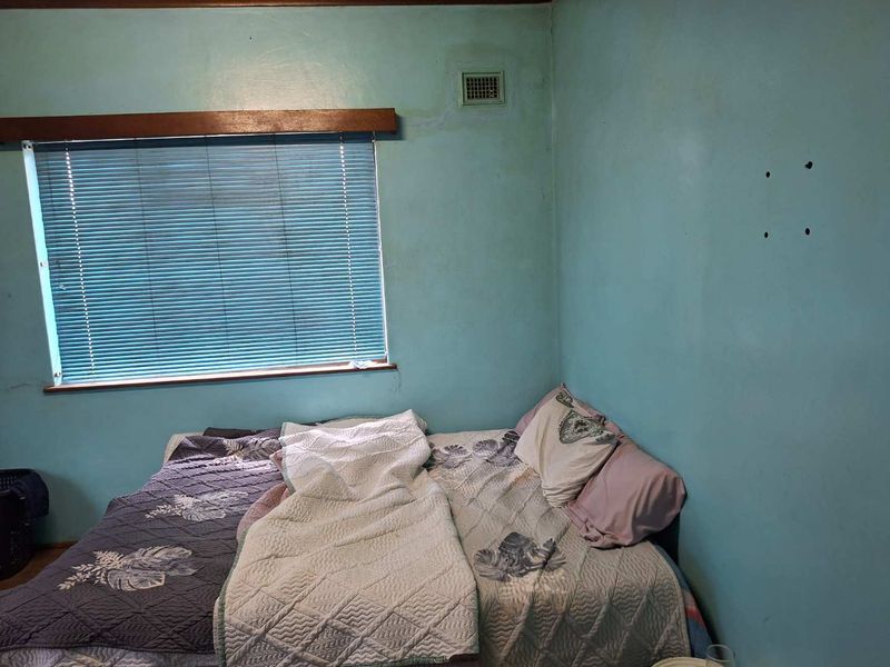 A bedroom featuring blue painted walls with visible surface wear and damage, including a window with fitted venetian blinds.