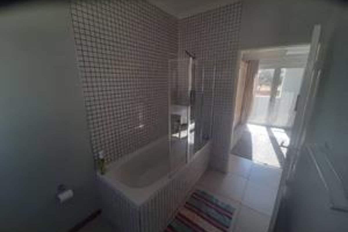 A functional bathroom featuring a built-in bathtub with a glass shower screen and mosaic wall tiling.