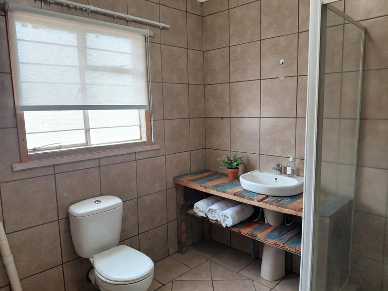 A functional bathroom featuring full-height ceramic wall tiling, a shower enclosure, a toilet, and a custom wooden vanity with a countertop basin.