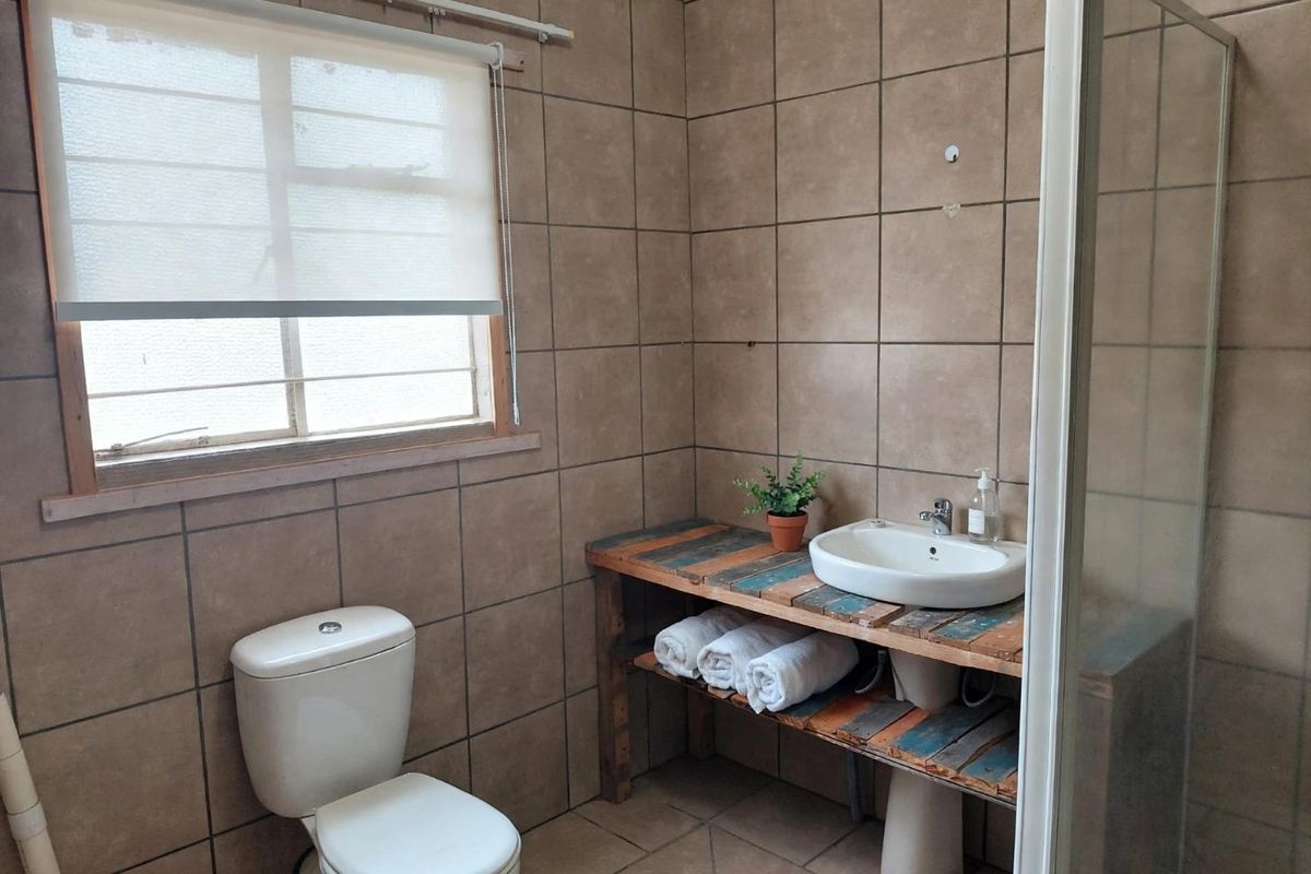 A functional bathroom featuring full-height ceramic wall tiling, a shower enclosure, a toilet, and a custom wooden vanity with a countertop basin.
