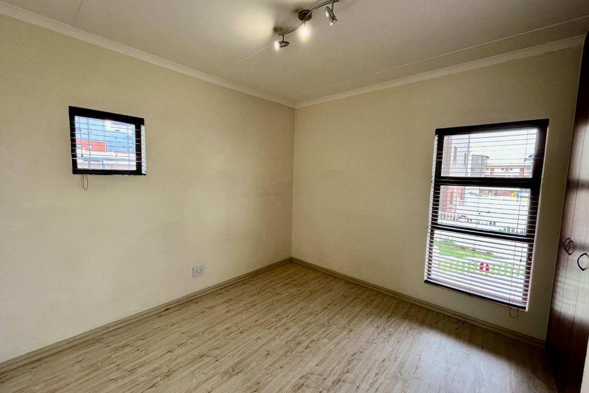 A clean, empty bedroom featuring light-toned laminate flooring, built-in storage, and venetian blinds on the windows, providing a neutral canvas for personalization.