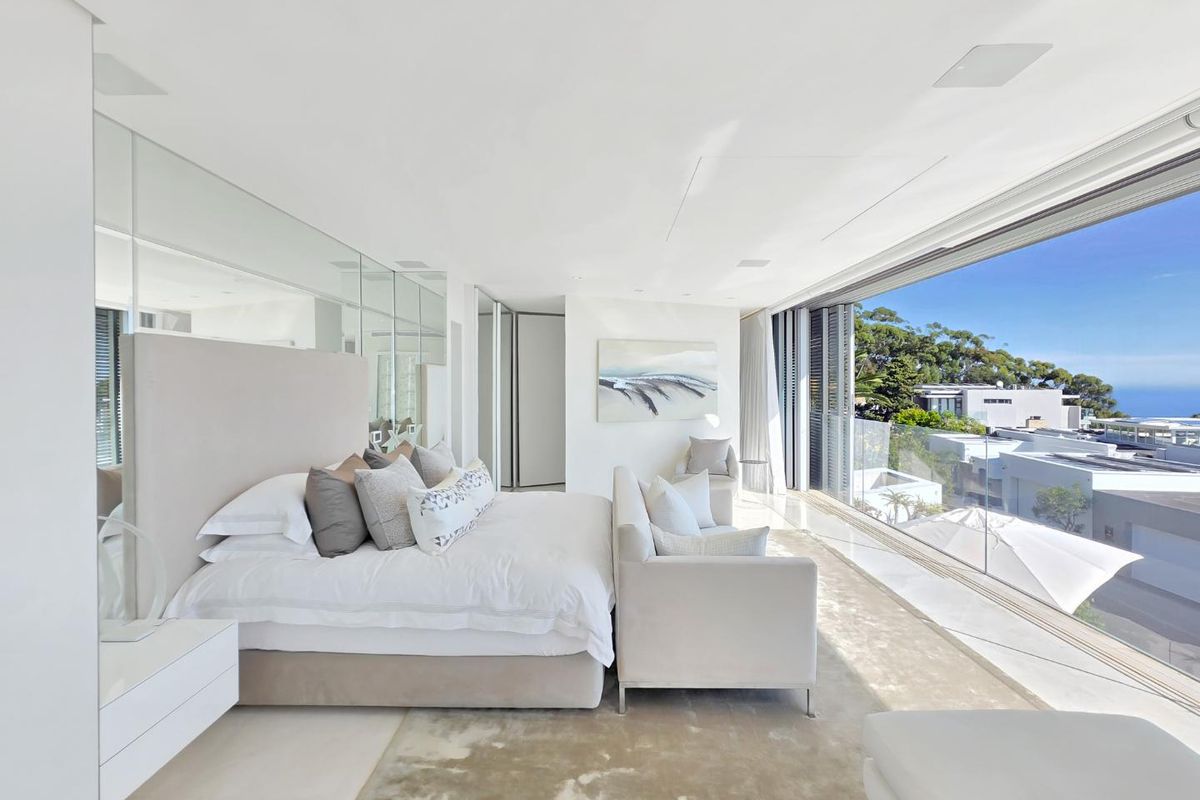 A bright, modern bedroom featuring floor-to-ceiling glass sliding doors that open to a balcony with expansive coastal and neighbourhood views.