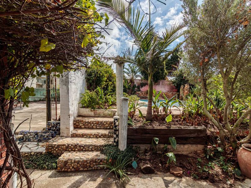 A garden area featuring stone-clad stairs, a retaining wall, and a glimpse of a swimming pool in the background.