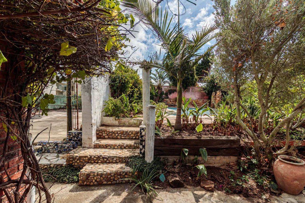 A garden area featuring stone-clad stairs, a retaining wall, and a glimpse of a swimming pool in the background.