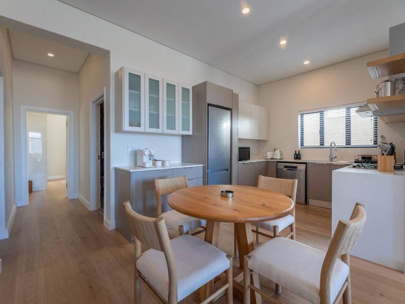 Modern open-plan kitchen and dining area featuring sleek cabinetry, stone countertops, integrated appliances, and light timber flooring throughout.