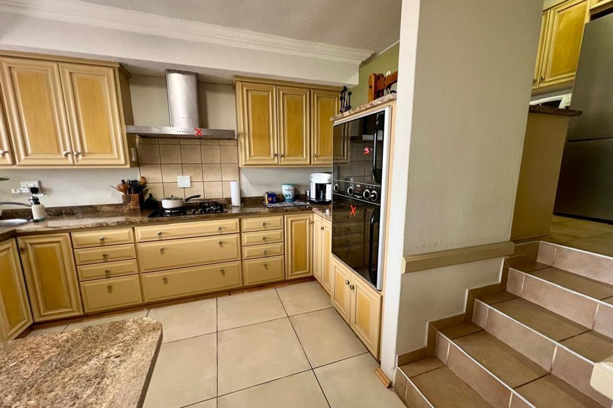 A functional kitchen featuring light wood cabinetry, granite countertops, a built-in oven, and a stainless steel extractor fan, with tiled flooring and adjacent stairs.