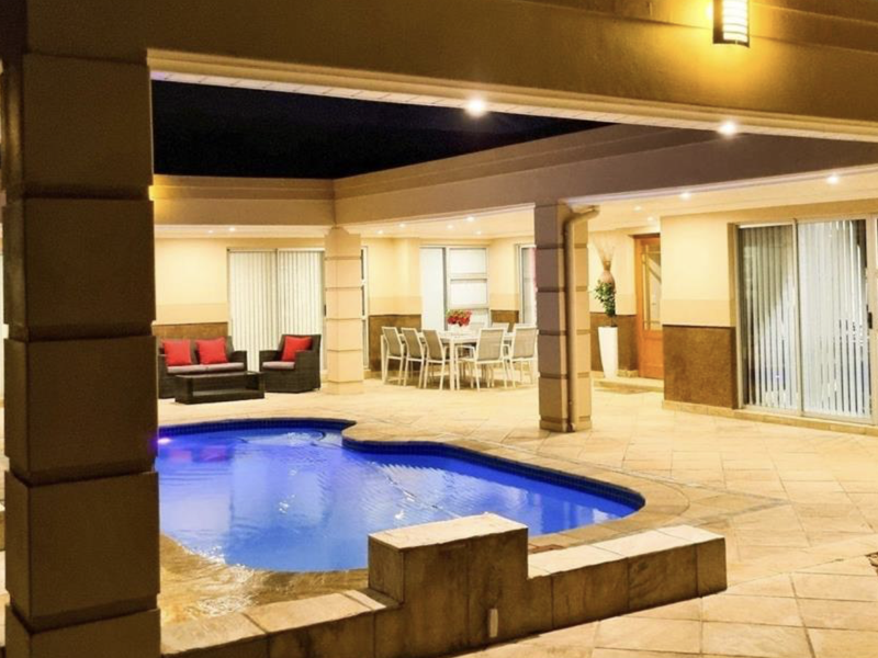 A well-lit covered patio area featuring a swimming pool, tiled flooring, and direct access to the home through multiple sliding glass doors.