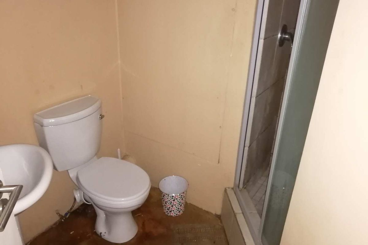 A compact bathroom featuring a pedestal basin, toilet, and a shower enclosure, currently requiring cosmetic updates and floor maintenance.