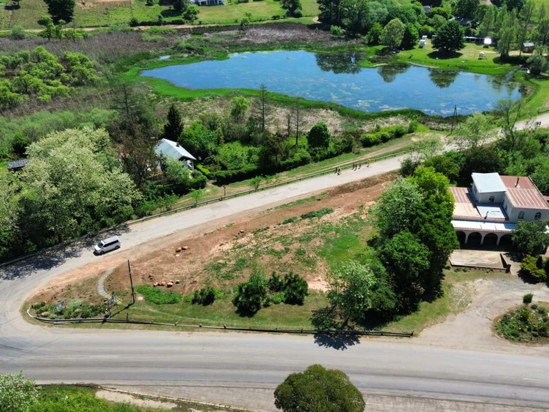 Aerial view of a vacant commercial land parcel featuring road frontage and proximity to a scenic pond.