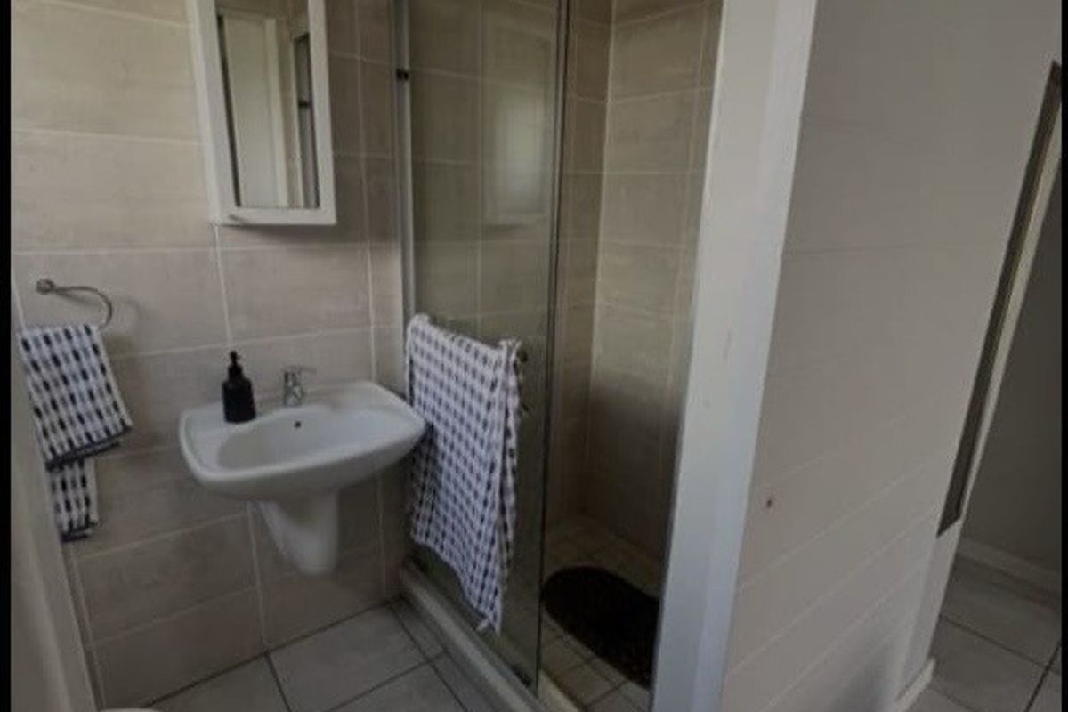 A functional bathroom featuring a pedestal basin, a glass-enclosed shower, and neutral ceramic wall and floor tiling.