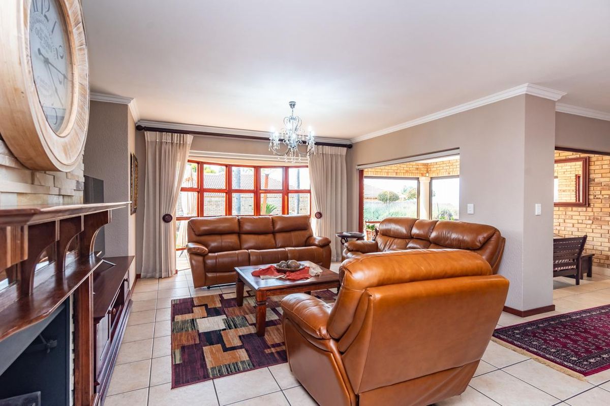 Spacious living room featuring tiled flooring, crown molding, and a stone-clad fireplace, with large windows providing natural light and access to the patio.