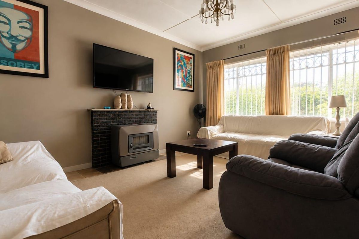 A comfortable living room featuring a brick fireplace, neutral wall tones, and large windows fitted with security bars.