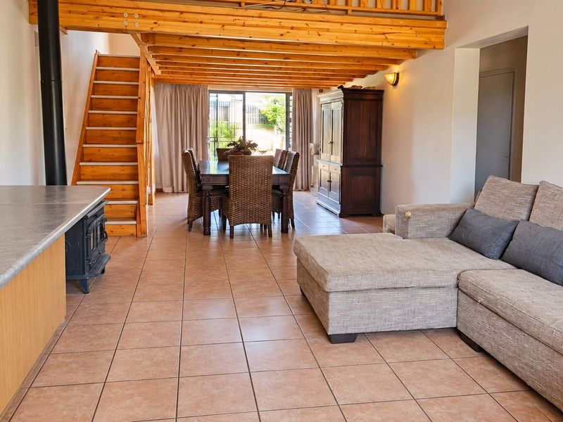 Open-plan living area featuring tiled floors, exposed timber beams, a wood-burning fireplace, and a staircase leading to a mezzanine level.