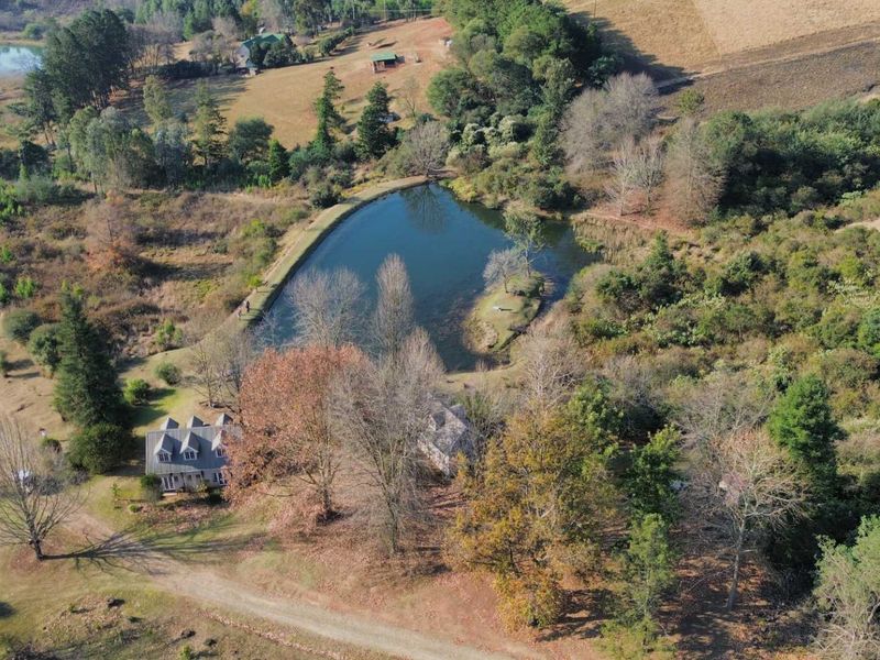 Aerial view of the farm property featuring a private dam, established trees, and expansive natural landscape with gravel access roads.