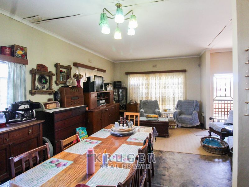 Open plan living and dining area featuring large windows with security bars and visible ceiling damage requiring repair.