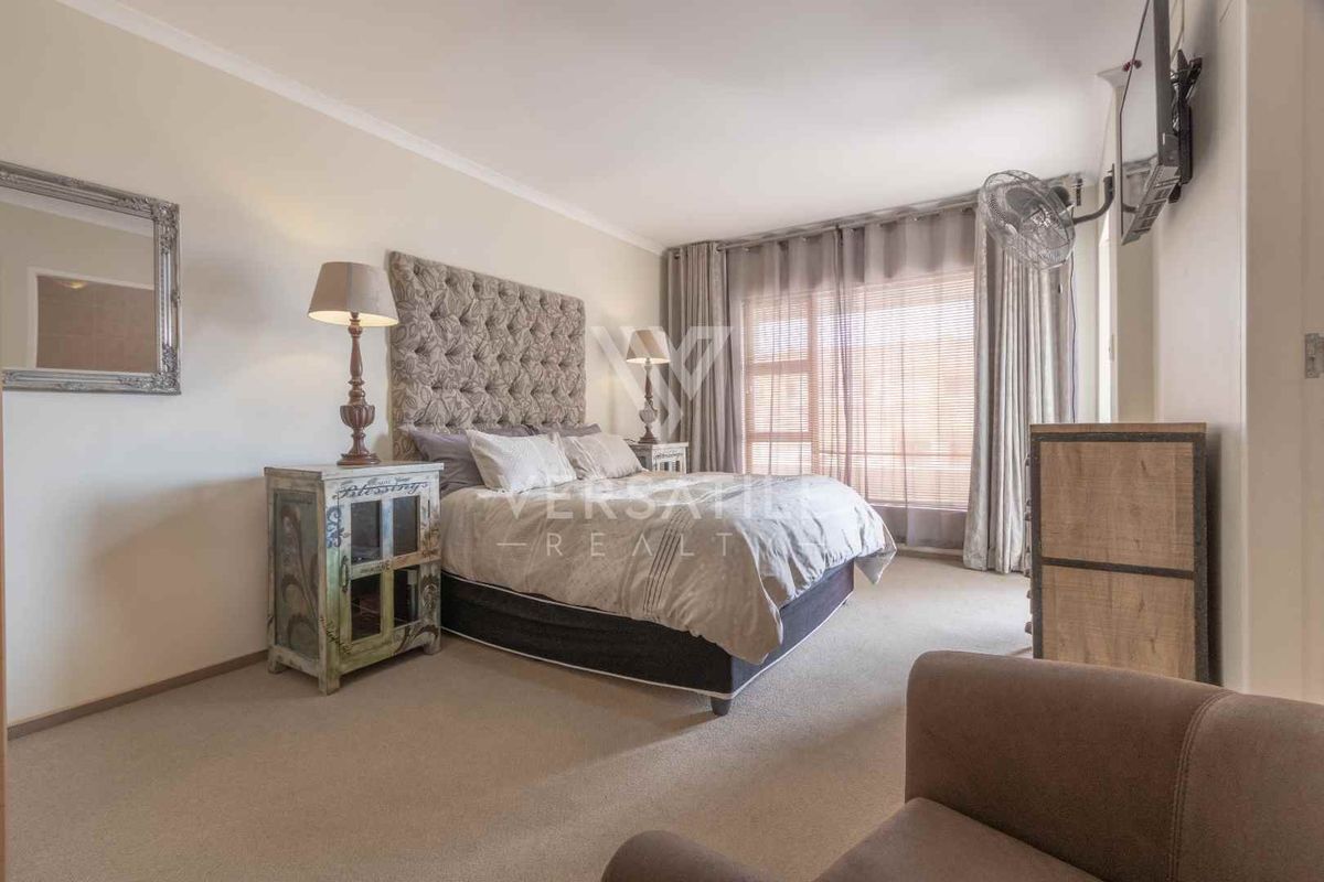 A well-lit bedroom featuring neutral carpeting, large windows with curtain tracks, and a wall-mounted television bracket.