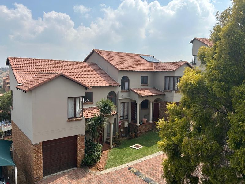 Elevated view of a multi-story townhouse featuring a tiled roof, solar panels, brick driveway, and a private garage entrance.