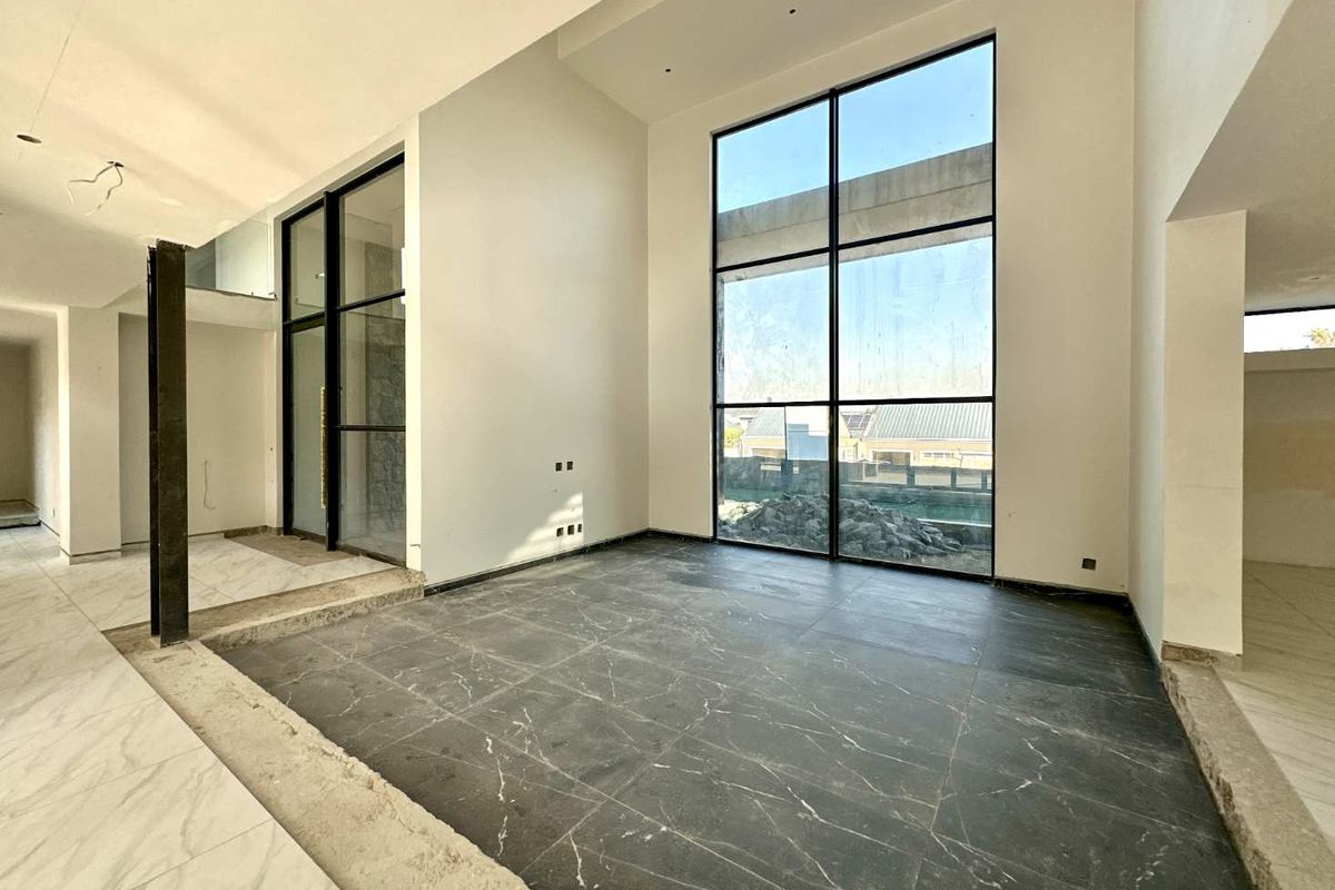 Spacious, double-volume living area featuring dramatic floor-to-ceiling windows, dark marble-look tiling, and a sunken floor design, currently in an unfinished state.
