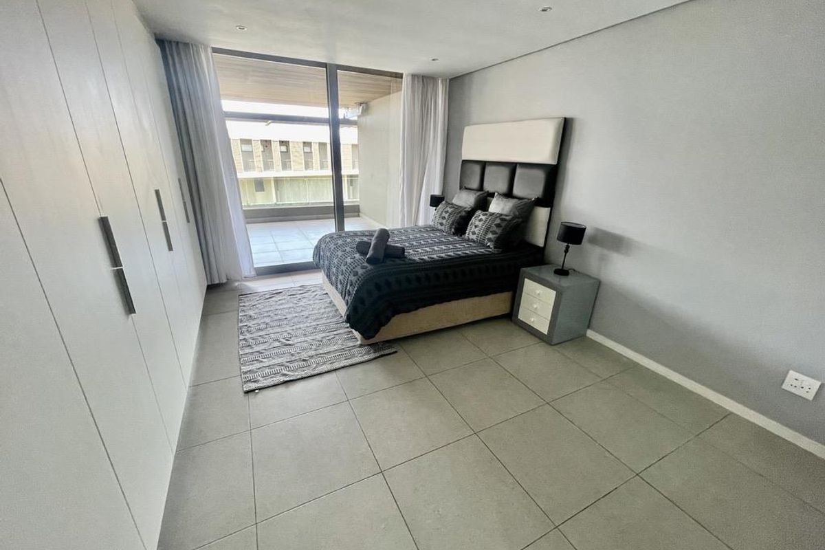 Modern bedroom featuring large format floor tiles, extensive built-in cabinetry, and floor-to-ceiling sliding glass doors opening onto a private balcony.