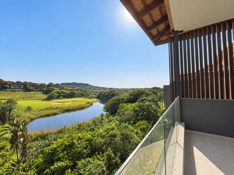 A modern balcony featuring a glass balustrade and timber privacy screen, offering scenic views over the surrounding landscape and golf course.