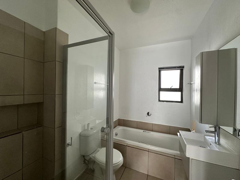 A clean, functional bathroom featuring a shower enclosure, bathtub, vanity basin, and neutral tiling throughout.
